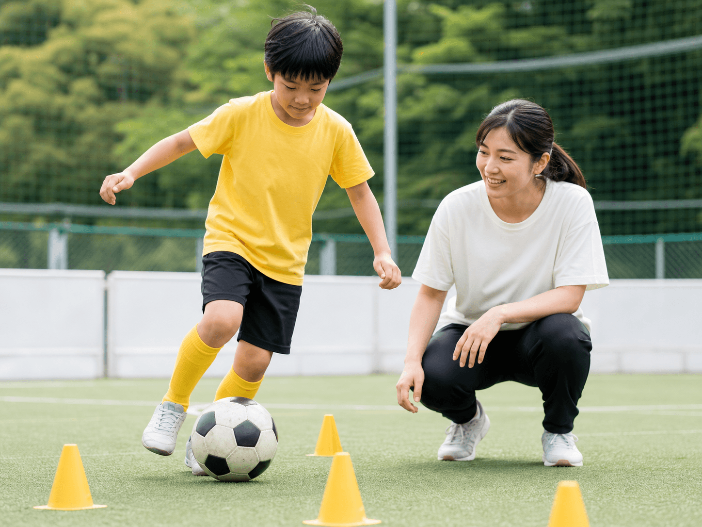 スタッフが見守る中でサッカーに取り組む子どものイメージ